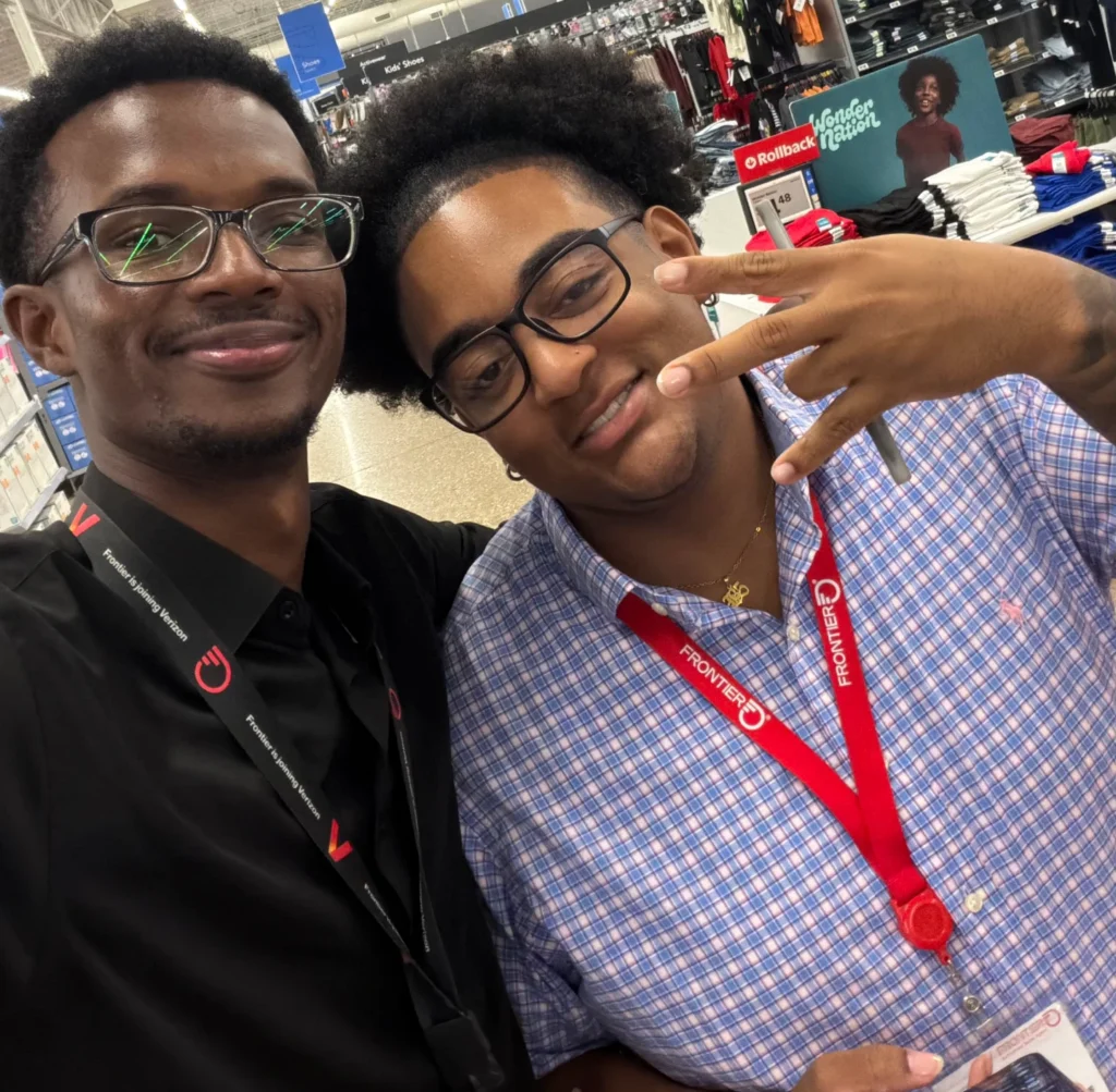 Two smiling individuals pose together in a retail store, showcasing their employee badges and friendly demeanor.